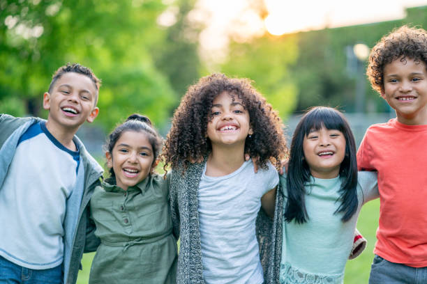 Outdoor Children's Portrait A small group of diverse children stand side-by-side outdoors in a park as they pose for a portrait.  They are each dressed casually and are smiling with their arms around one another. school children stock pictures, royalty-free photos & images