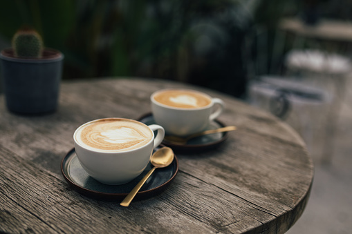 Two cups of hot cappuccino on a wooden table outdoors.