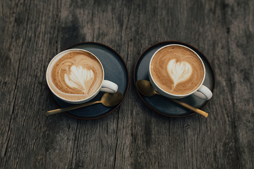 Two cups of fresh hot cappuccino on a wooden table outdoors.