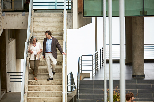 Full length front view of man and woman in early 40s side by side as they move down outdoor staircase on their way to class. Property release attached.