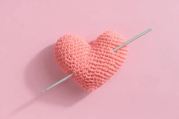 Crocheted amigurumi pink heart with crochet hook on a pink background. Valentine's day banner with a copyspace