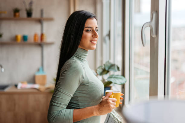 istock Young Woman Standing By The Window And Drinking Coffee 1455992636