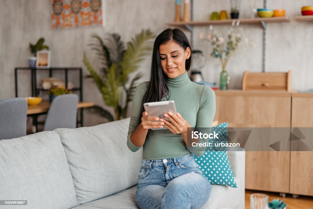 Young Woman Using Digital Tablet At Home Smiling young beautiful woman relaxing at home and using tablet. Adult Stock Photo