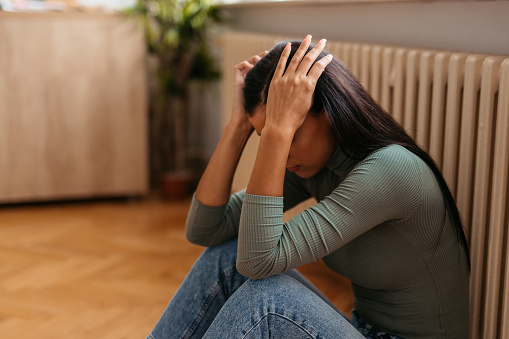 Sad young woman sitting on the floor at home.