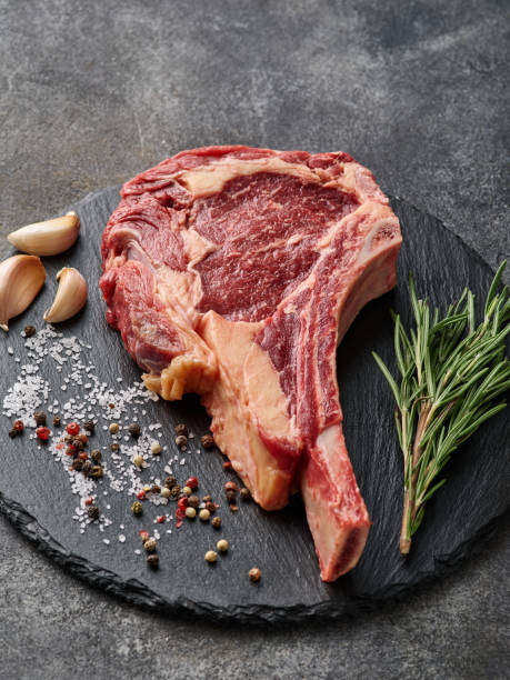 istock Raw dry aged beef tomahawk steak on slate board with spices for grill. 1455997342