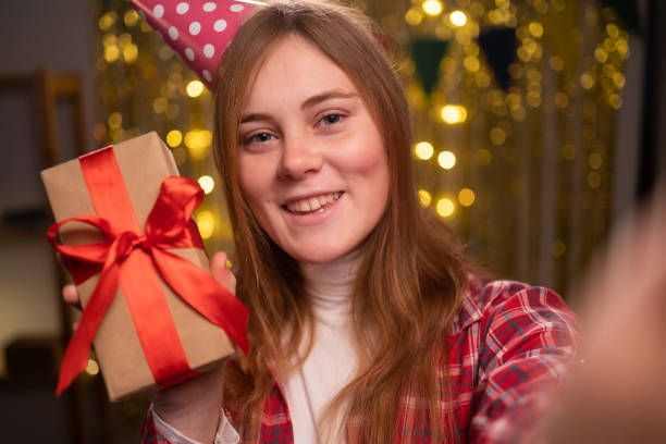 la foto della ragazza positiva tiene la scatola regalo fa selfie in piedi in casa al chiuso con la decorazione della festa di compleanno - 12 18 months foto e immagini stock