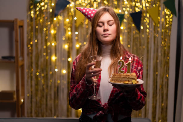 Caucasian girl makes a wish closing her eyes holding a birthday cake with candles number 21 in her hands Caucasian girl makes a wish closing her eyes holding a birthday cake with candles number 21 in her hands. Copy space 21st birthday stock pictures, royalty-free photos & images