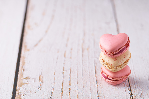 Stack of three heart shaped cream filled French macaroons on white wooden background. Traditional confections for Valentine's Day, Mother's Day, wedding or romantic love. Closeup with pastel colors.