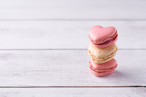 Stack of three heart shaped cream filled French macaroons on white wooden background. Traditional confections for Valentine's Day, Mother's Day, wedding or romantic love. Closeup with pastel colors.