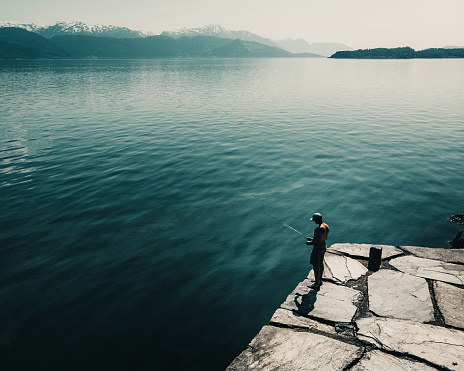 A man fishing on the edge of a lake standing on a rocky ground