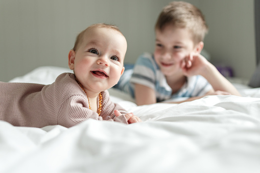 Cute baby girl lying on the bed whit her brother at home