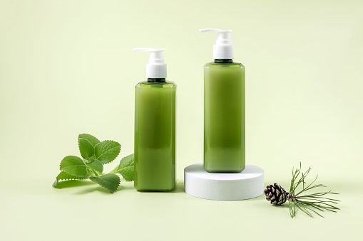 containers for cosmetics on the podium, a sprig of mint, a pine cone and a pine branch on a light green background