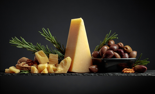 Parmesan cheese with olives and rosemary on a black background.