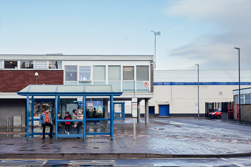 A wide angle front view of a male couple and their children waiting for the bus in a town centre in Blyth in the North East of England. They have two sons and one daughter in their blended family.