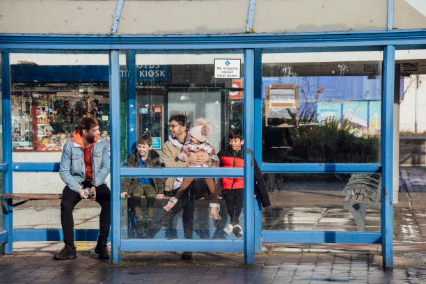 A medium close front view of a male couple and their children waiting for the bus in a town center in Blyth in the North East of England. They have two sons and one daughter in their blended family and the young daughter is sitting on her fathers knee.
