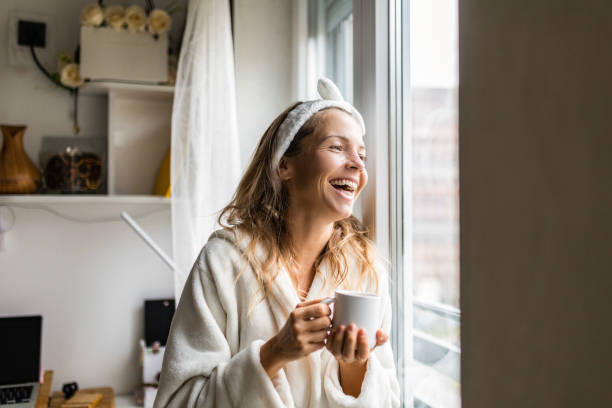 istock Smiling attractive young woman at home drinking coffee looking through window 1456007447