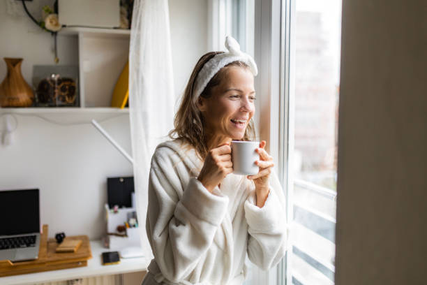 istock Woman at home drinking coffee looking through window 1456007539