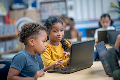 A small group of elementary students sit at their desks with personal laptops in front of each one as they work during a computer lab.  They are each dressed casually and are focused on their work.