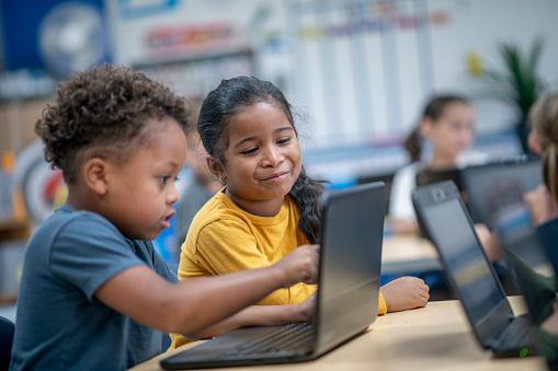 A small group of elementary students sit at their desks with personal laptops in front of each one as they work during a computer lab.  They are each dressed casually and are focused on their work.