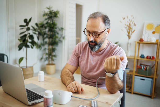 Mature man checking blood pressure while having online meeting with a doctor stock photo