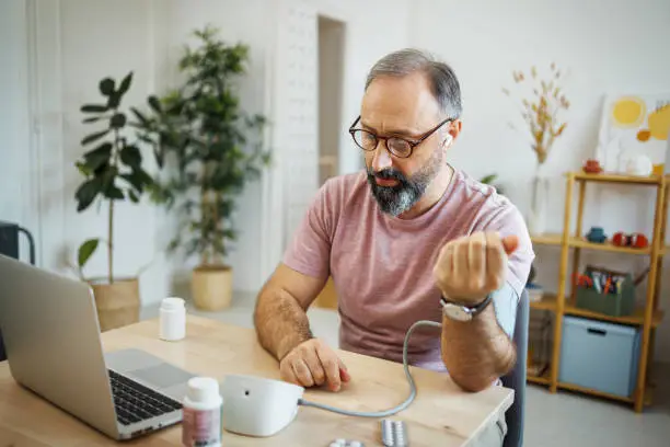 Photo of Mature man checking blood pressure while having online meeting with a doctor