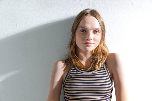 A blonde and freckled girl on a white background, wearing a striped brown t-shirt. Studio with sunlight.