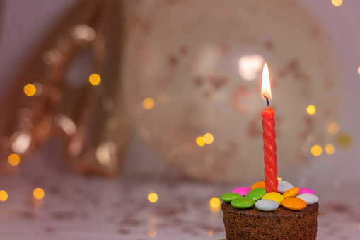 Birthday party with cupcakes on burning candle. With balloons and lights on bokeh background