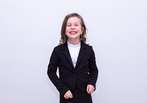 Portrait of a Caucasian schoolgirl girl 7 years old in a black jacket, smiling happily and looking at the camera.