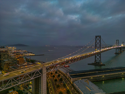 Aerial view of the Bay Bridge as the sun comes up. Bridge is illuminated and the morning traffic is visible.