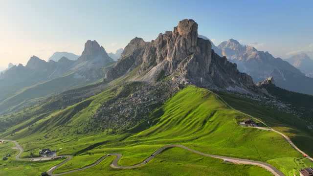 Panoramic aerial drone flight video around trekker on green hill with beautiful sunset scene summer of Dolomites Alps mountain landscape. Stunning Giau Pass - 2236m mountain pass in the province of Belluno in Italy