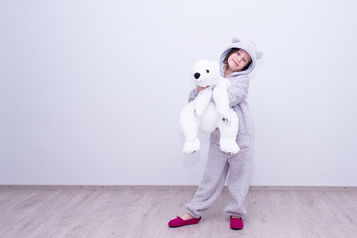 Portrait of a Caucasian girl 7 years old in warm home clothes smiles happily and looks at the camera and hugs a soft toy, a polar bear.