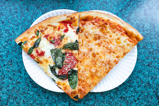An overhead view of two delicious margherita and cheese New York City style slices on white paper plates