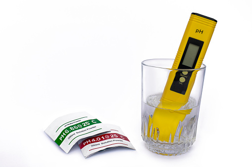 pH meter measuring the pH of the water in the glass on isolated white background. used solution solution packages.