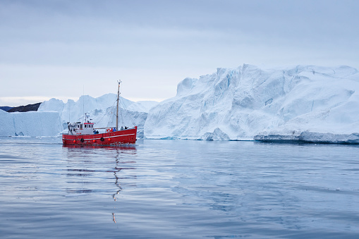 small boat sailing near big icebergs in artic polar circle