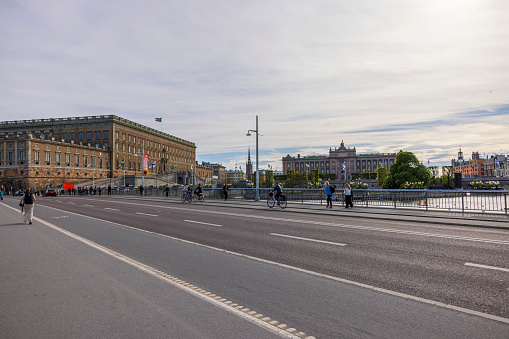 Sweden, Europe. 05.18.2022. Beautiful view from bridge to Royal Palace of Stockholm, bicycles  passing and people walking on bridge over river.