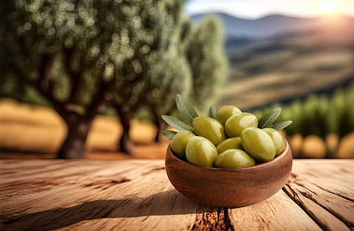 Delicious olives in wooden bowl on olive plantation background