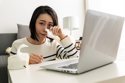 young pretty Asian woman sitting on a cozy sofa in the living room while using her laptop.