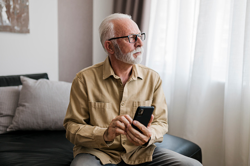 Serious Elderly man grandfather using smart phone, searching web, loading feed, social media. Communication with children, grandchildren on lockdown