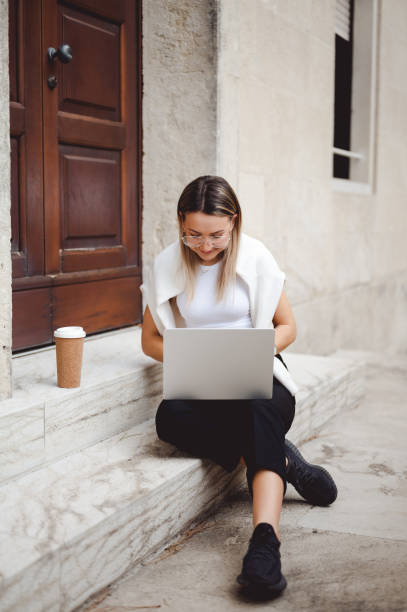 istock Busy young woman working on laptop computer outdoors, sitting on a stairs. 1456021560