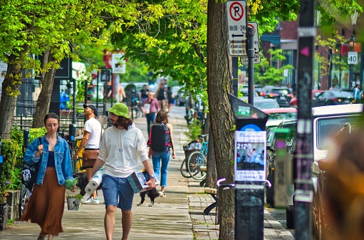 Montreal, Canada – May 15, 2022: A group of people walking on a sidewalk on a busy street in Montreal on a beautiful day