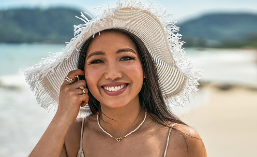Asian woman wearing fashion summer beach hat for skin care sun protection. Beauty portrait on summer vacation travel. Smiling girl looking at the camera.