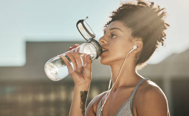 runner, fitness e acqua potabile per donne con podcast audio online per l'allenamento o l'allenamento in città. donna nera, musica in streaming e cardio o idratazione sana dopo lo sport eseguito all'aperto - human settlement audio foto e immagini stock