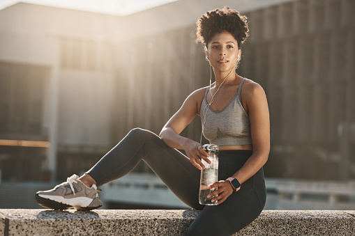 Fitness, earphones and black woman, water bottle break and training workout, exercise and motivation in urban city. Thinking young athlete, sports hydration and nutrition for body, wellness and goals