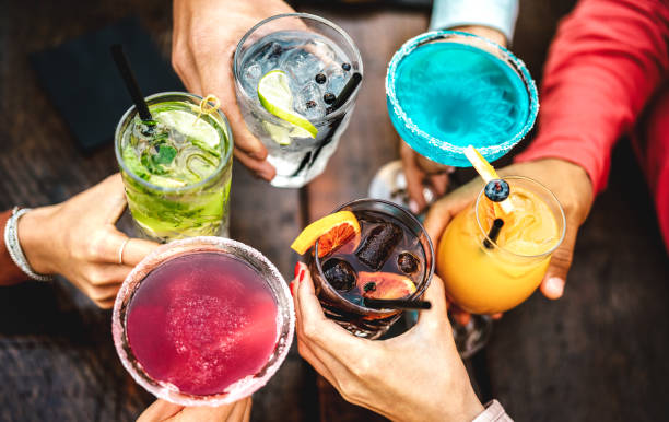 Top view of people hands toasting multicolored fancy drinks - Young friends having fun drinking cocktails at happy hour - Social gathering party concept on vivid filter - Shallow depth of field stock photo