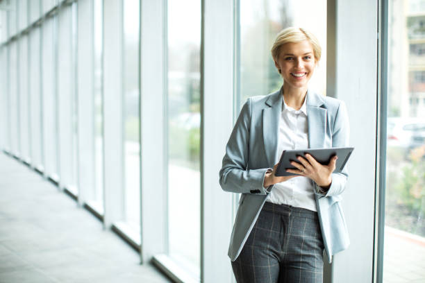 Jeune femme d’affaires blonde travaillant sur une tablette numérique à l’intérieur d’un bâtiment moderne - Photo