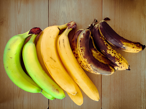 Bananas of different stages of ripening on wooden surface