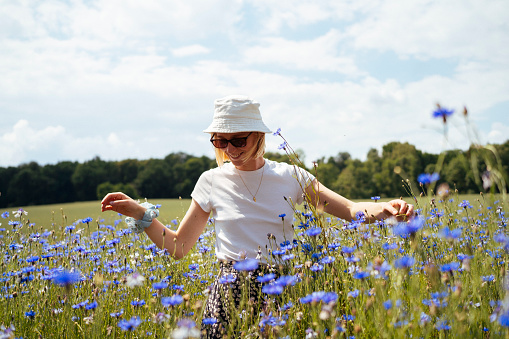 A young woman stands tall among a sea of blue cornflowers, embracing the natural beauty of the field on a sunny summer day.