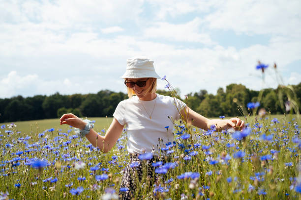 Young woman in a sea of blue cornflowers A young woman stands tall among a sea of blue cornflowers, embracing the natural beauty of the field on a sunny summer day. bucket hat stock pictures, royalty-free photos & images