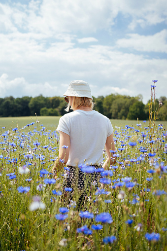 A young woman stands in a beautiful field of blue cornflowers, taking in the natural beauty of the meadow on a sunny summer day.