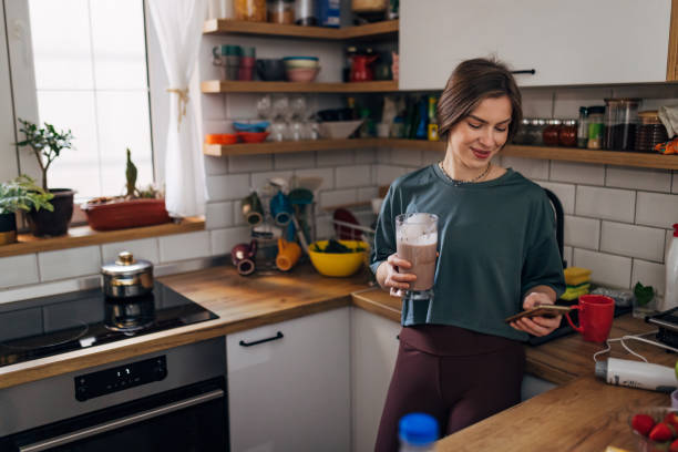 donna dell'atleta che beve frappè per spuntino e usando lo smartphone - blueberry smoothie milk shake drink foto e immagini stock